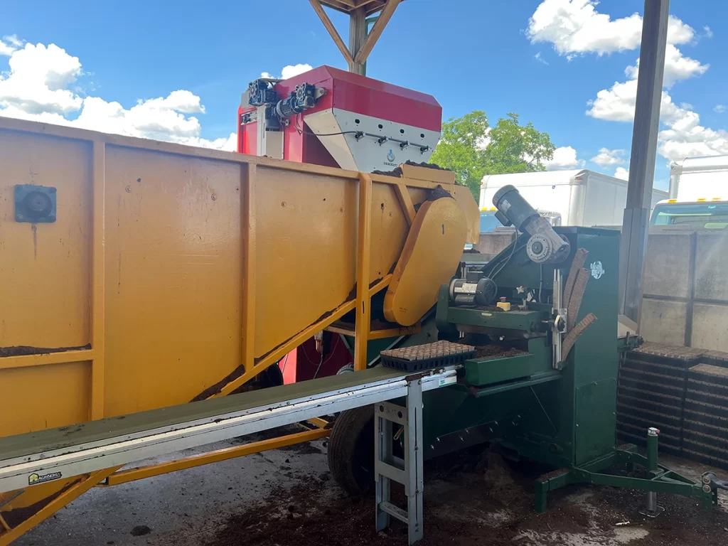 Industrial plant potting machine with conveyor belts and mechanical components, crucial for efficient plant processing at the nursery.
